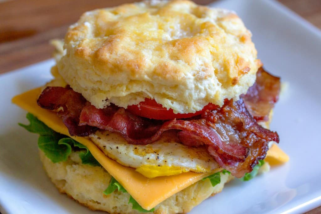 Bacon, egg, and cheese biscuit sandwich with tomato and lettuce on a plate